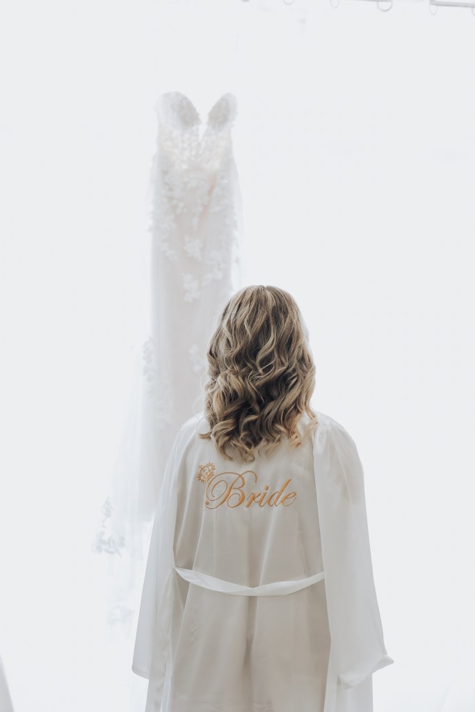 Mariée de dos en peignoir Bride face à sa robe suspendue