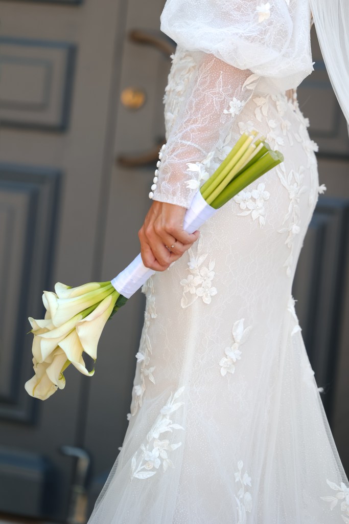 Mariée tenant un bouquet de callas contre sa robe en dentelle