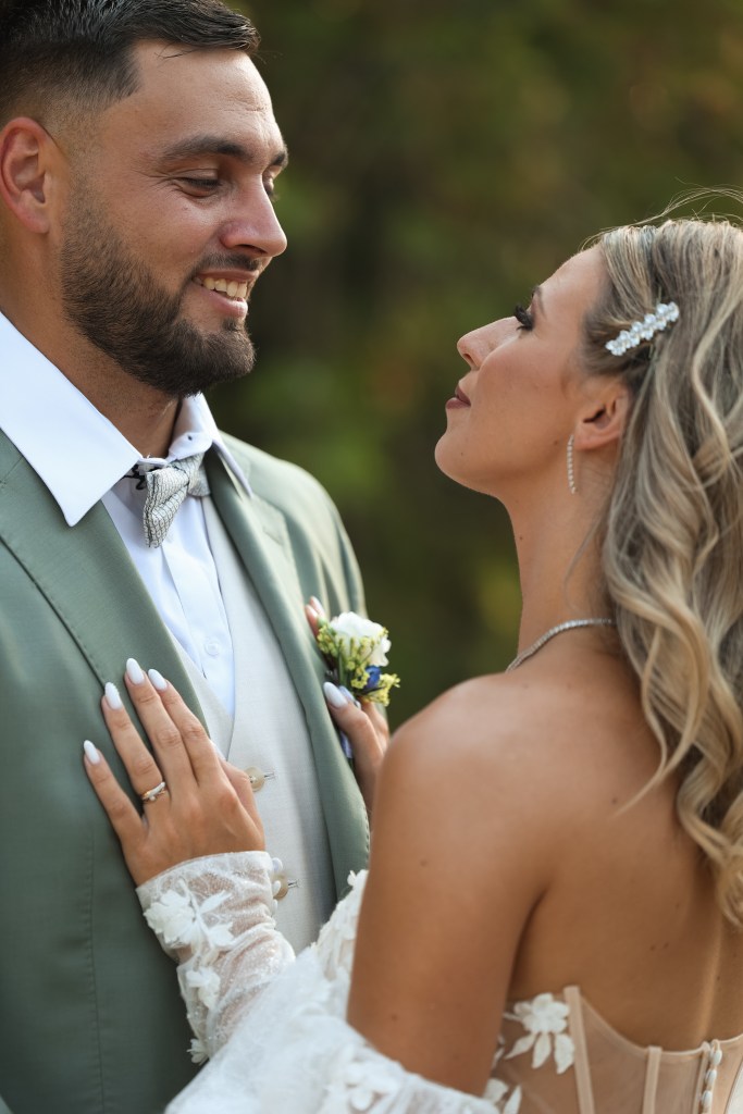 Mariés face à face, la mariée pose la main sur le costume vert sauge